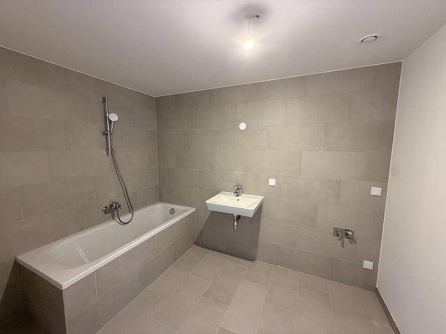 Modernes Badezimmer mit Badewanne, Waschtisch und Fliesenboden in neutralen Farben.