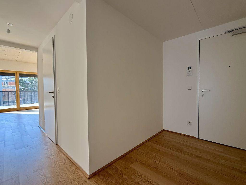 Heller Flur mit Holzboden und weißen Wänden, der zu den Wohnbereichen führt.