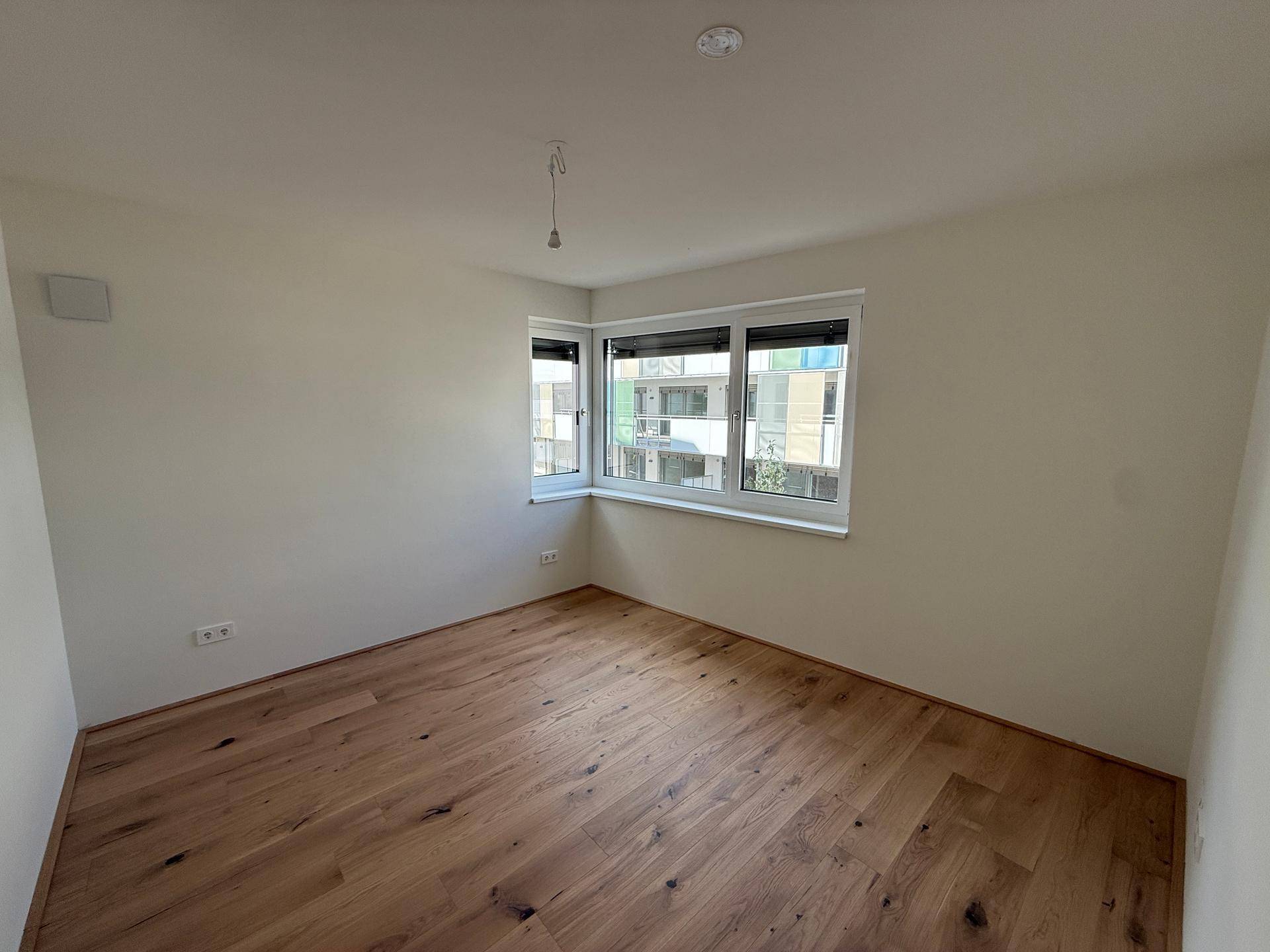 Helles, leeres Schlafzimmer mit Holzboden und Eckfenstern, bereit zur Gestaltung.