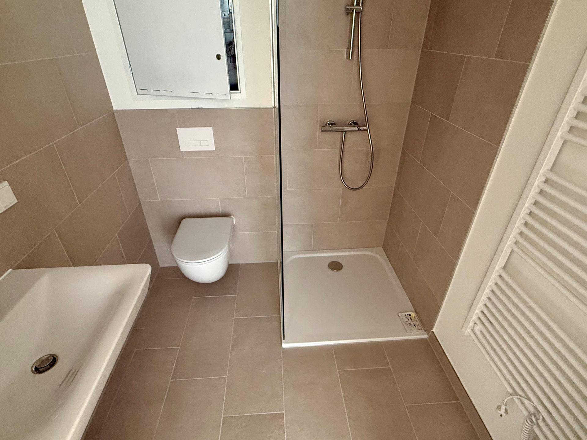 Zeitgemäßes Badezimmer mit ebenerdiger Dusche, WC und Waschbecken, in neutralen Beigetönen gehalten.