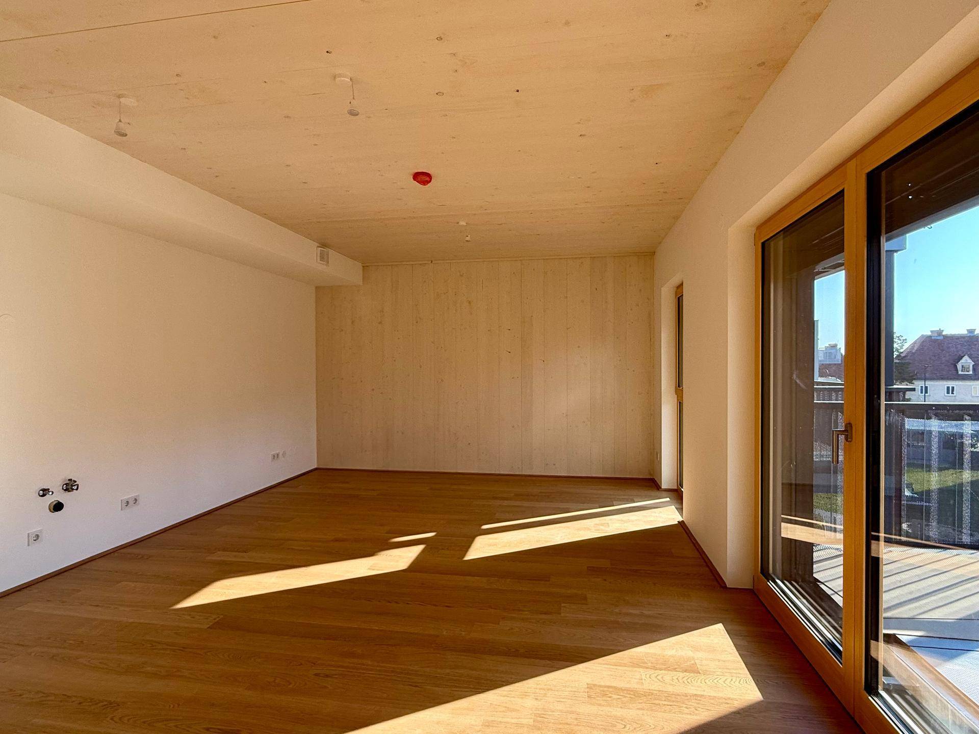 Lichtdurchfluteter Wohnbereich mit Holzboden und unverputzter Holzwand, ideal für individuelle Gestaltung.