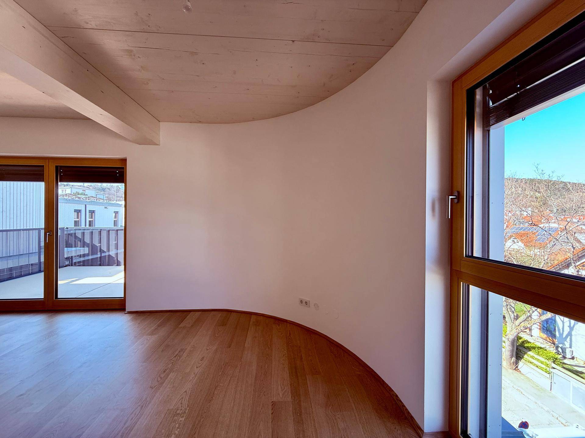 Geräumiger Wohnbereich mit Holzboden, großen Fenstern und einer geschwungenen Wand für modernes Design.