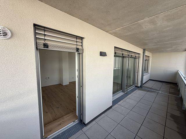 Geräumiger Balkon mit Fliesenboden und Blick auf die umliegenden Gebäude, ausgestattet mit Jalousien.