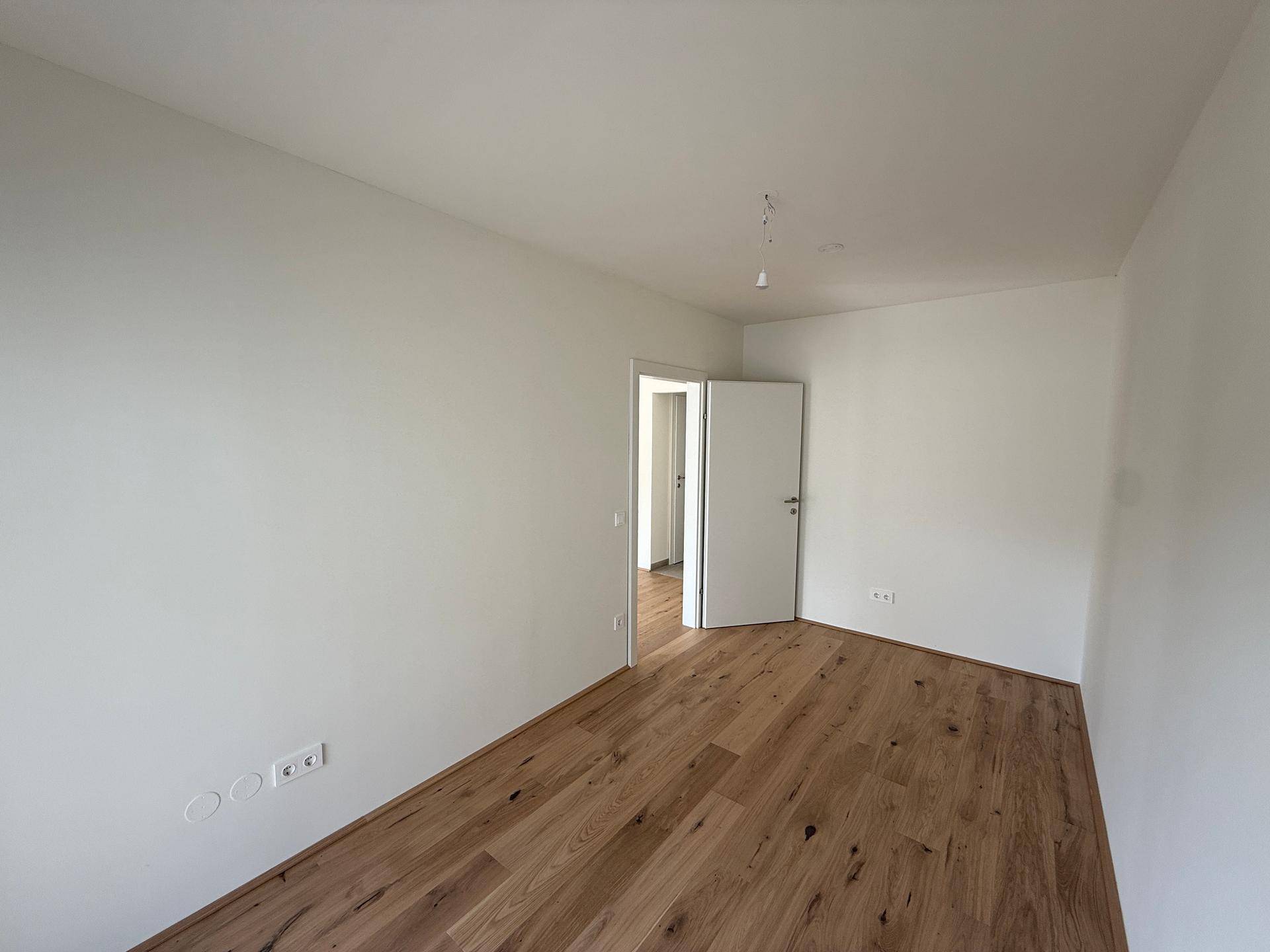 Heller, leerer Raum mit Holzboden und weiß gestrichenen Wänden, ideal als Schlafzimmer.