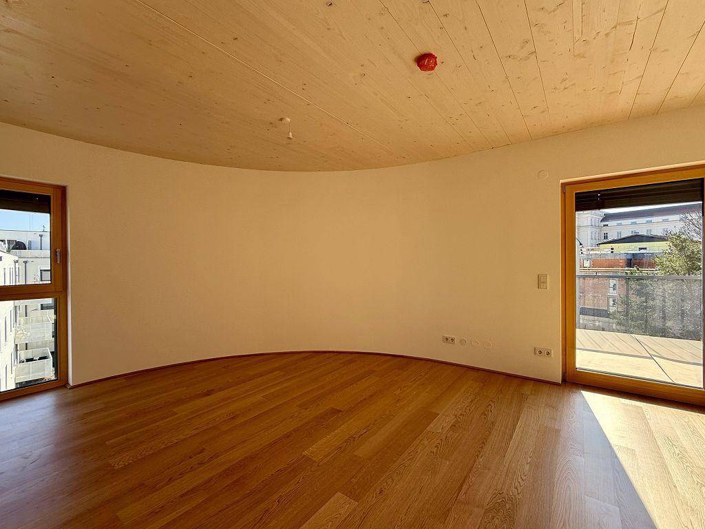 Heller Wohnraum mit geschwungener Wand, Holzboden und direktem Zugang zu einem Außenbereich.