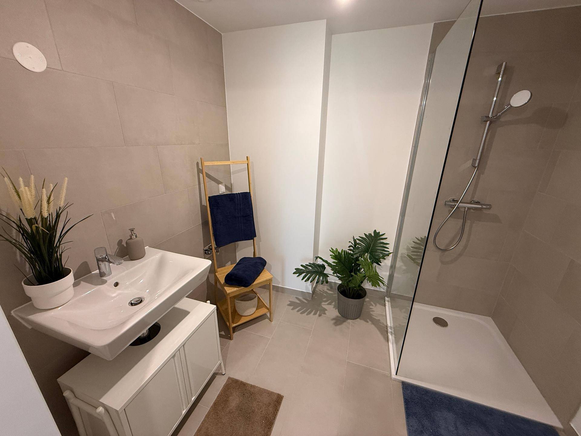 Modernes Badezimmer mit ebenerdiger Dusche, Einzelwaschbecken und hellgrauen Fliesen.