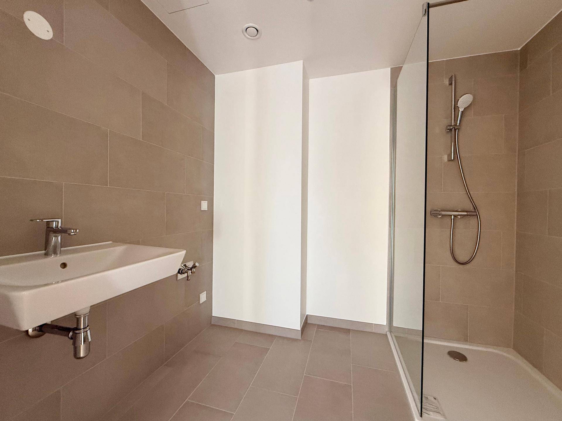 Modernes Badezimmer mit beigefarbenen Fliesen, Einzelwaschbecken und Glasdusche.