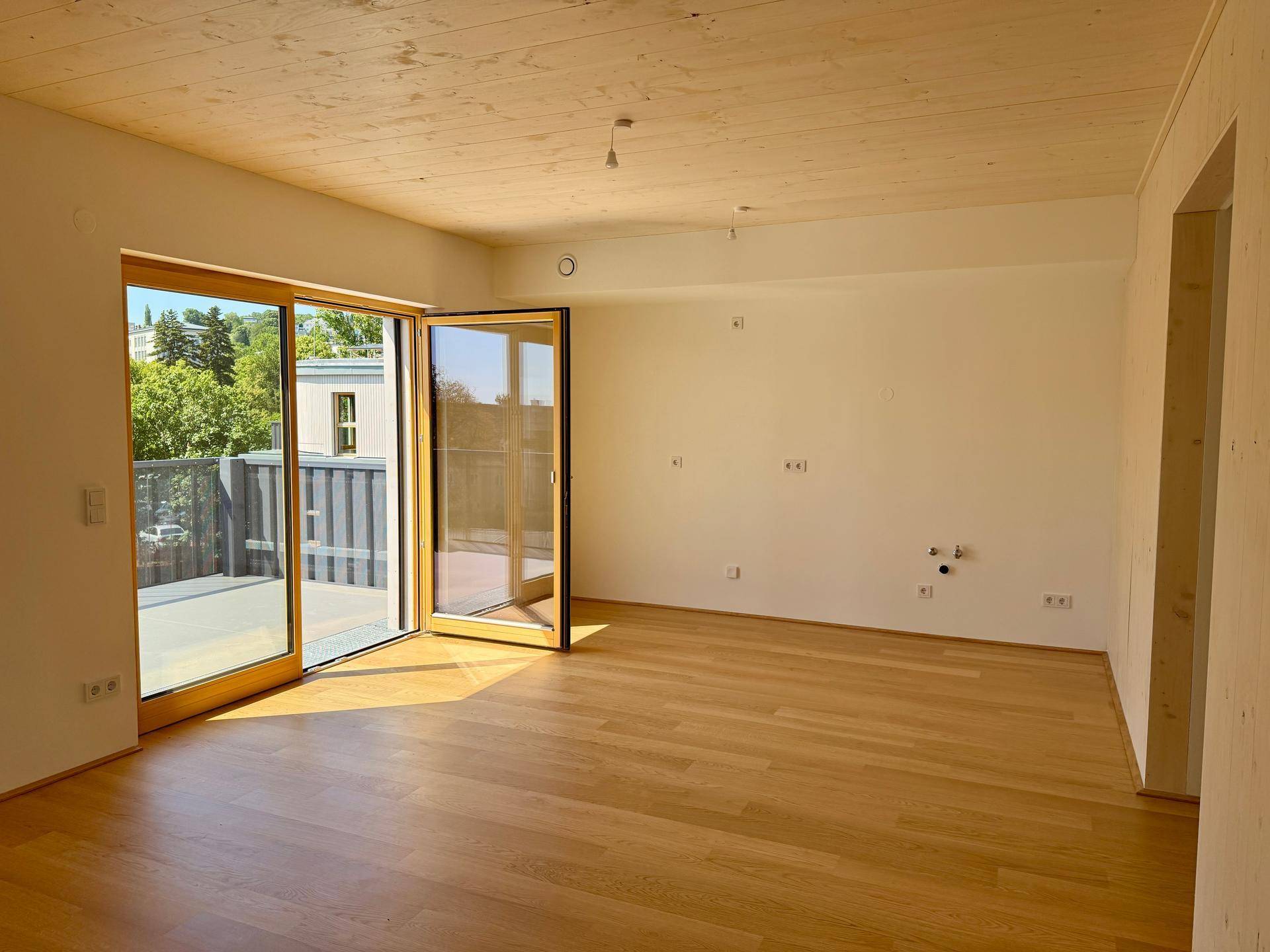 Lichtdurchfluteter Wohnraum mit hellem Holzparkett, Holzdecke und großem Balkonzugang.