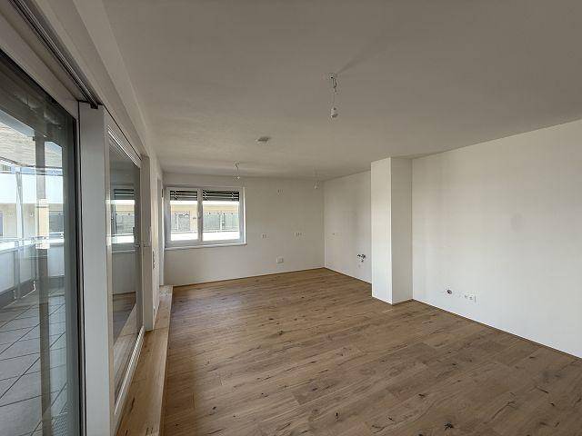 Heller, leerer Wohnraum mit Holzboden und Zugang zu einem Balkon, bereit zur individuellen Gestaltung.