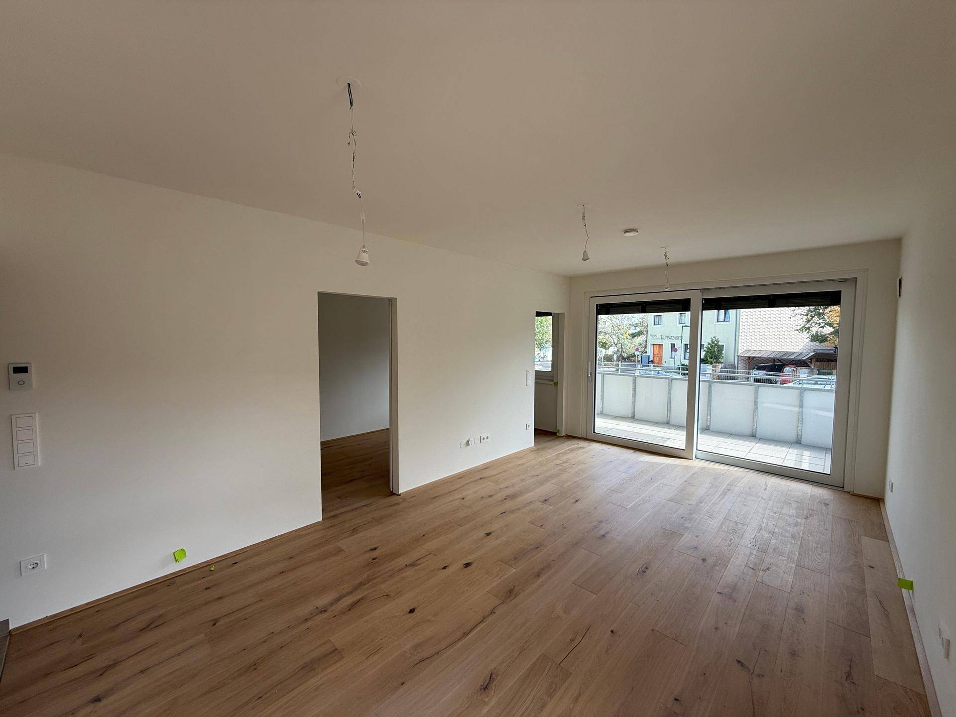 Helles, leeres Wohnzimmer mit neuem Holzparkettboden und Zugang zu einem Balkon.