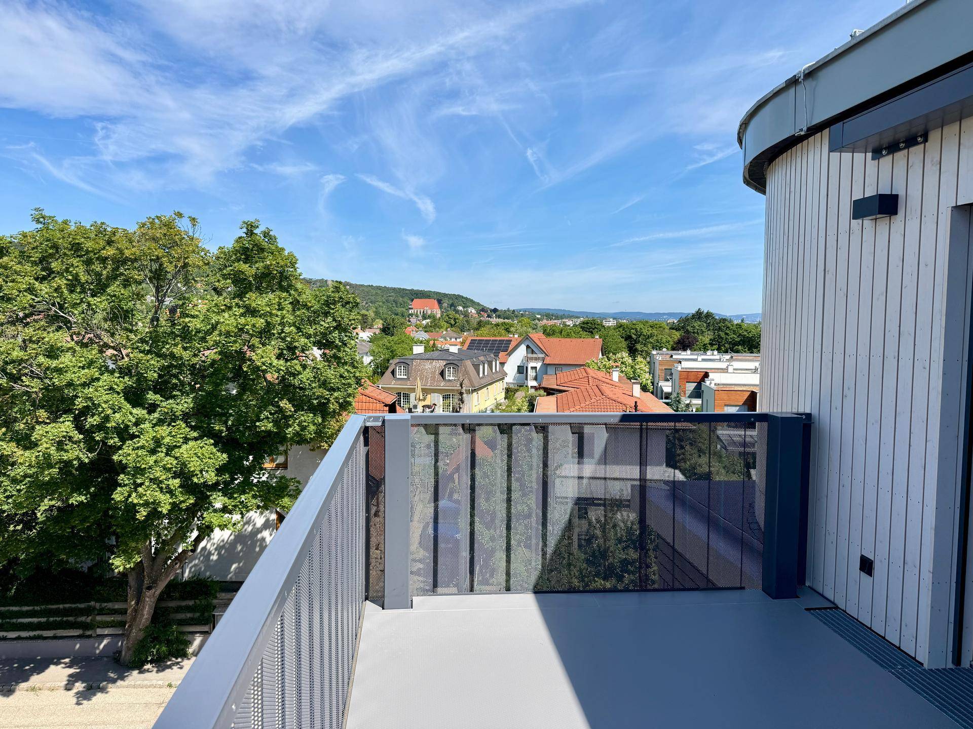 Sonniger Balkon mit Glasgeländer und Panoramablick auf die umliegende Wohngegend und Natur.