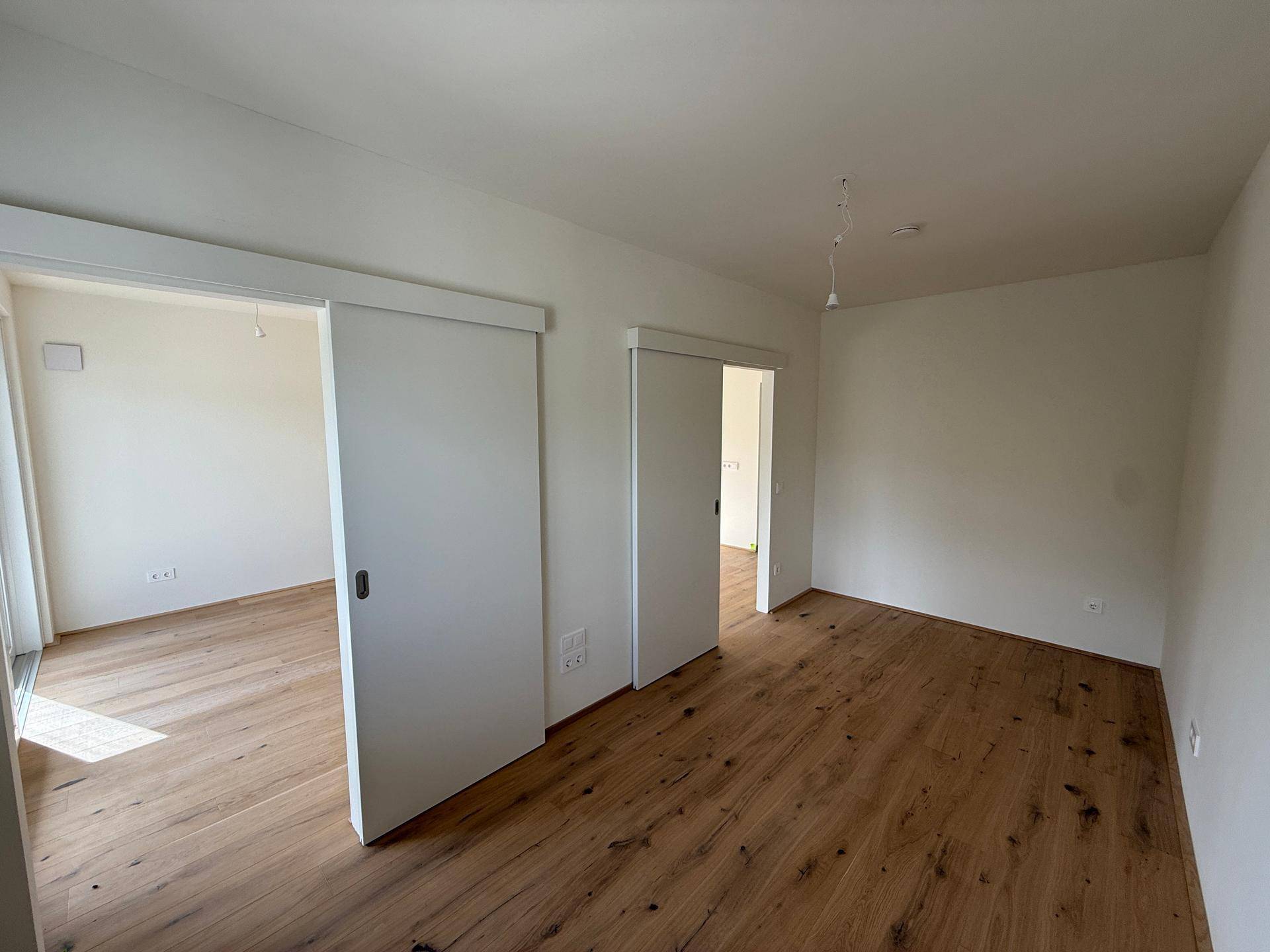 Heller Raum mit Holzboden und modernen Schiebetüren, die zu angrenzenden Bereichen führen.