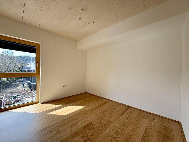 Geräumiges Schlafzimmer mit Holzboden, Holzbalkendecke und großem Fenster.