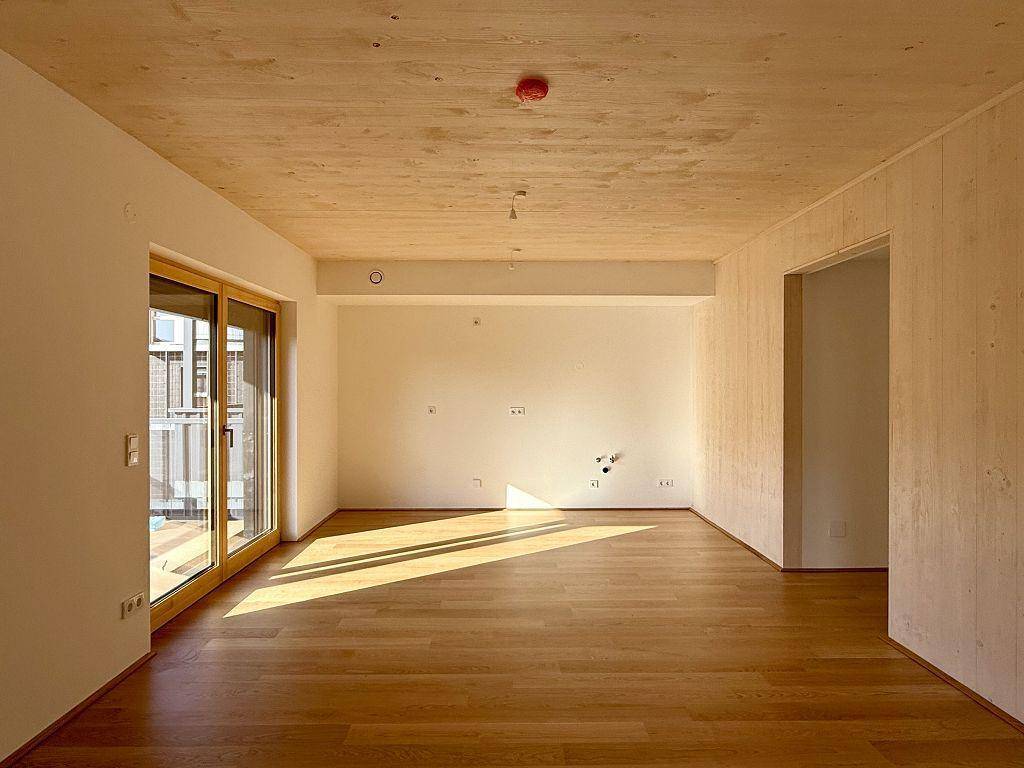Lichtdurchfluteter Raum mit Holzboden und einer Wand in Holzoptik, ideal für Wohnzwecke.
