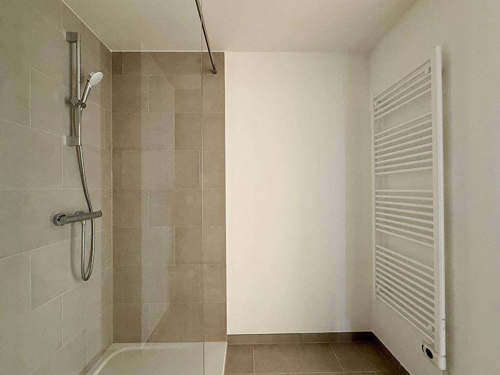 Duschbereich in einem modernen Badezimmer mit beigefarbenen Fliesen und Handtuchheizkörper.