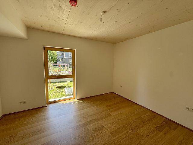 Geräumiges Schlafzimmer mit Holzboden und Fenster, das viel Tageslicht hereinlässt und eine grüne Aussicht bietet.