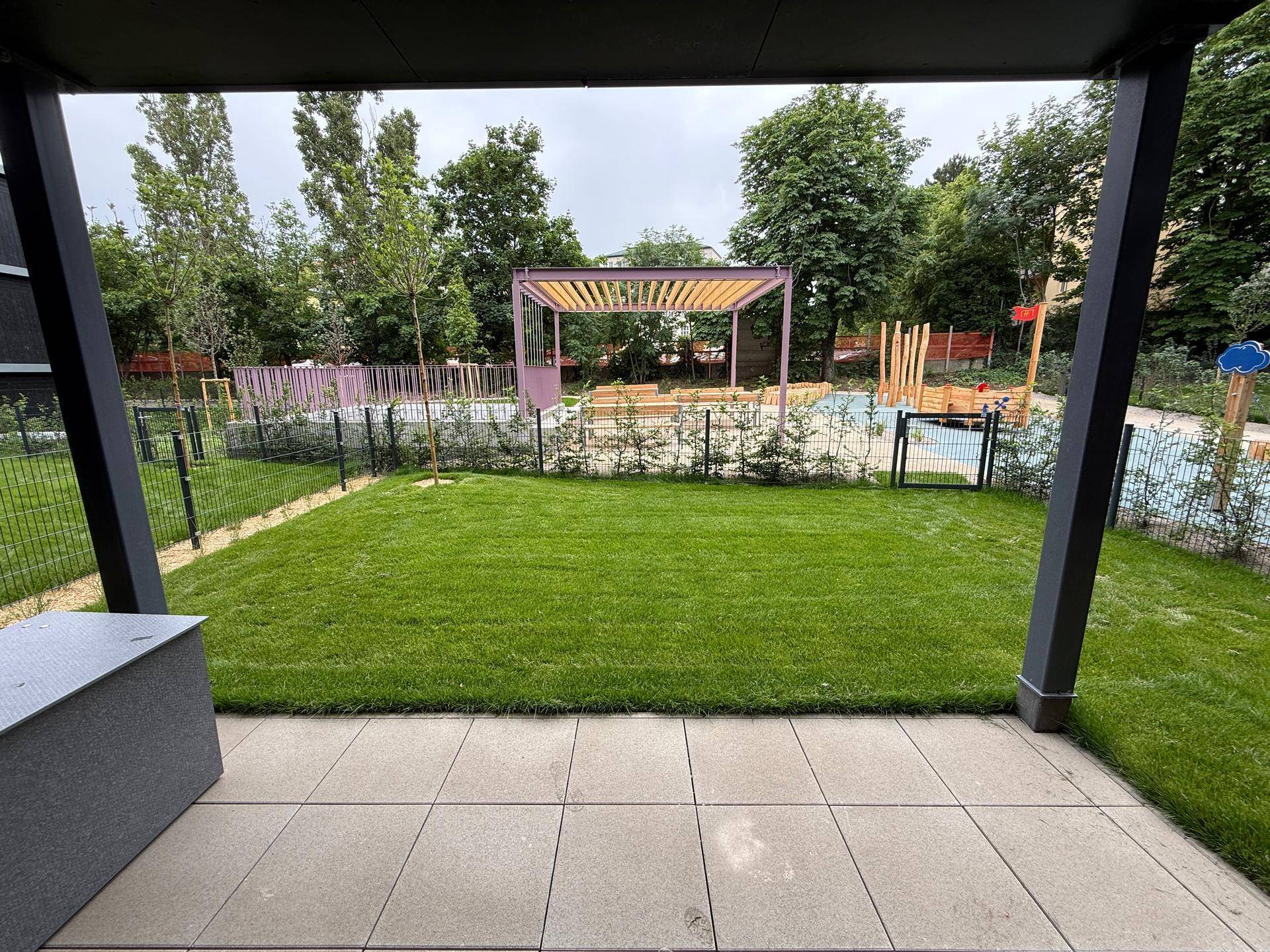 Geräumige Terrasse mit Blick auf einen grünen Rasen und den angrenzenden Kinderspielplatz.