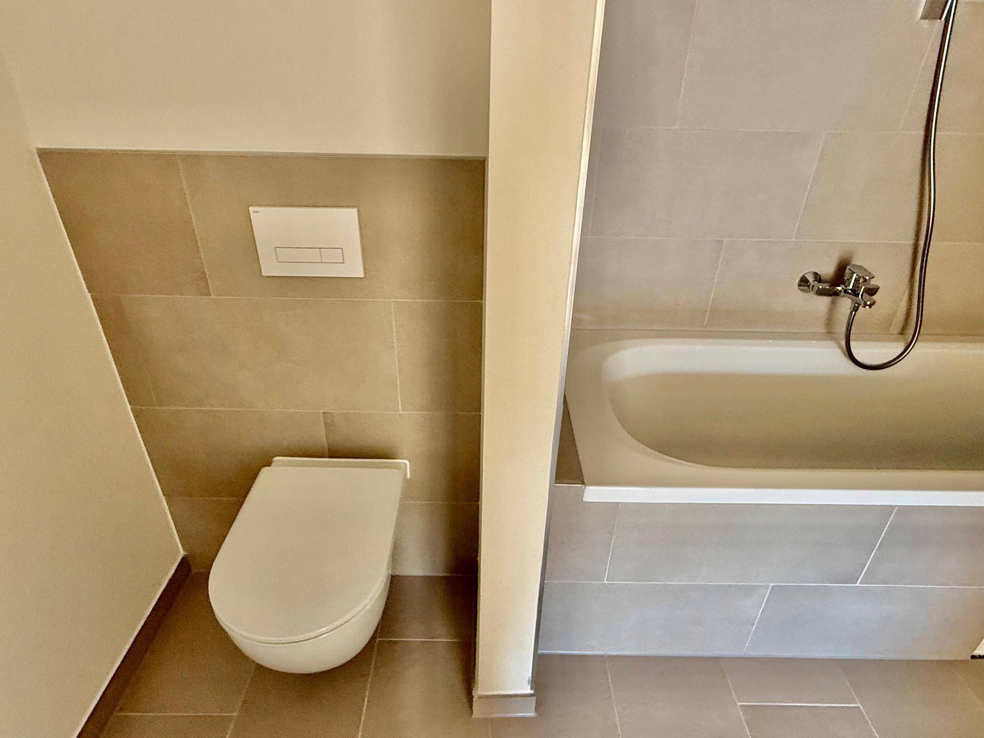 Badezimmer mit Badewanne und wandhängendem WC, gefliest in warmen Beigetönen für ein modernes Ambiente.