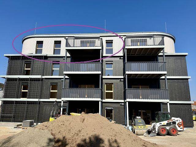 Neubau eines modernen Wohngebäudes mit dunkler Fassade, mehreren Balkonen und Baustelle im Vordergrund.