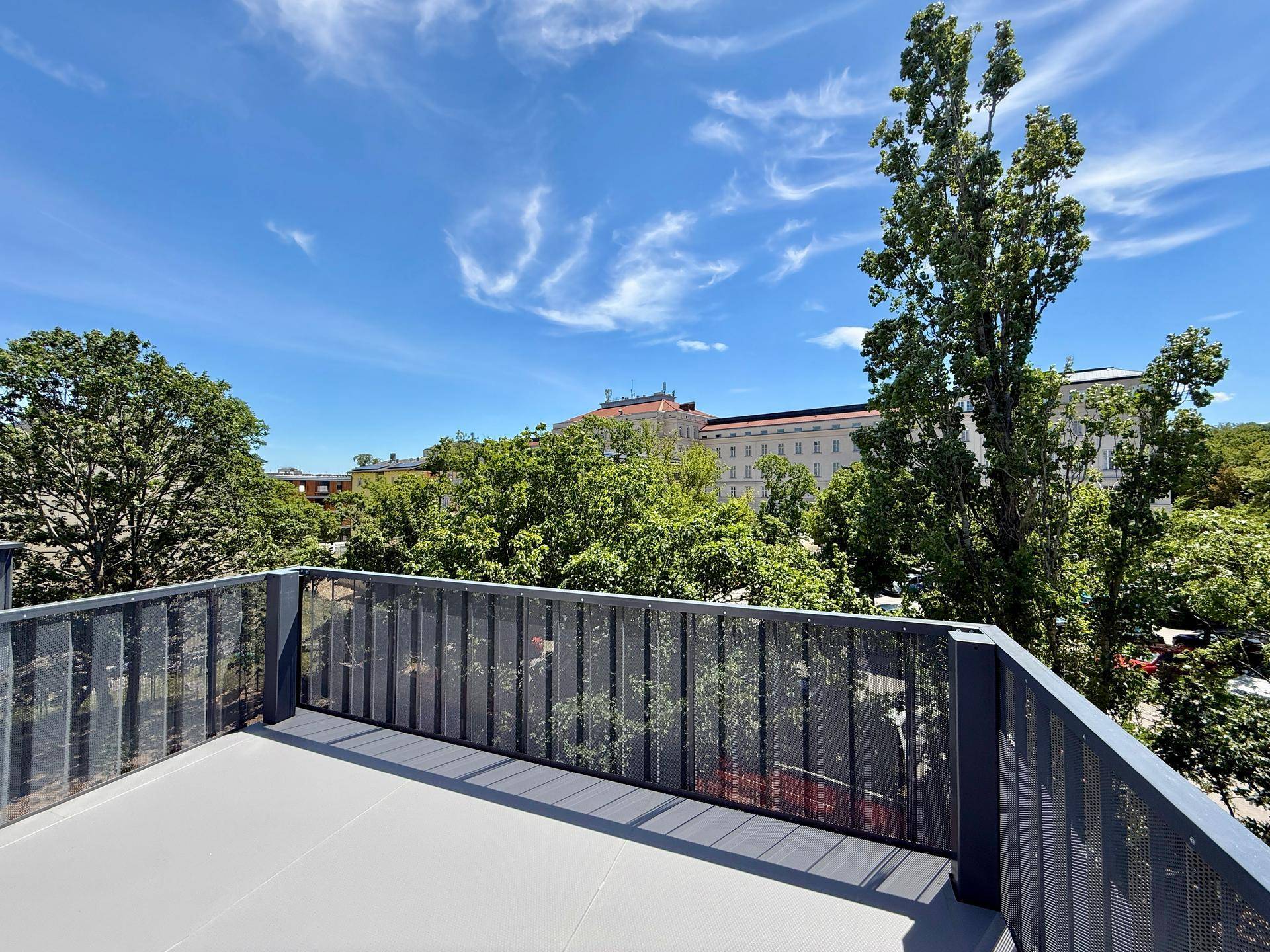 Sonniger Balkon mit Blick auf die Stadtbebauung und üppiges Grün unter blauem Himmel.