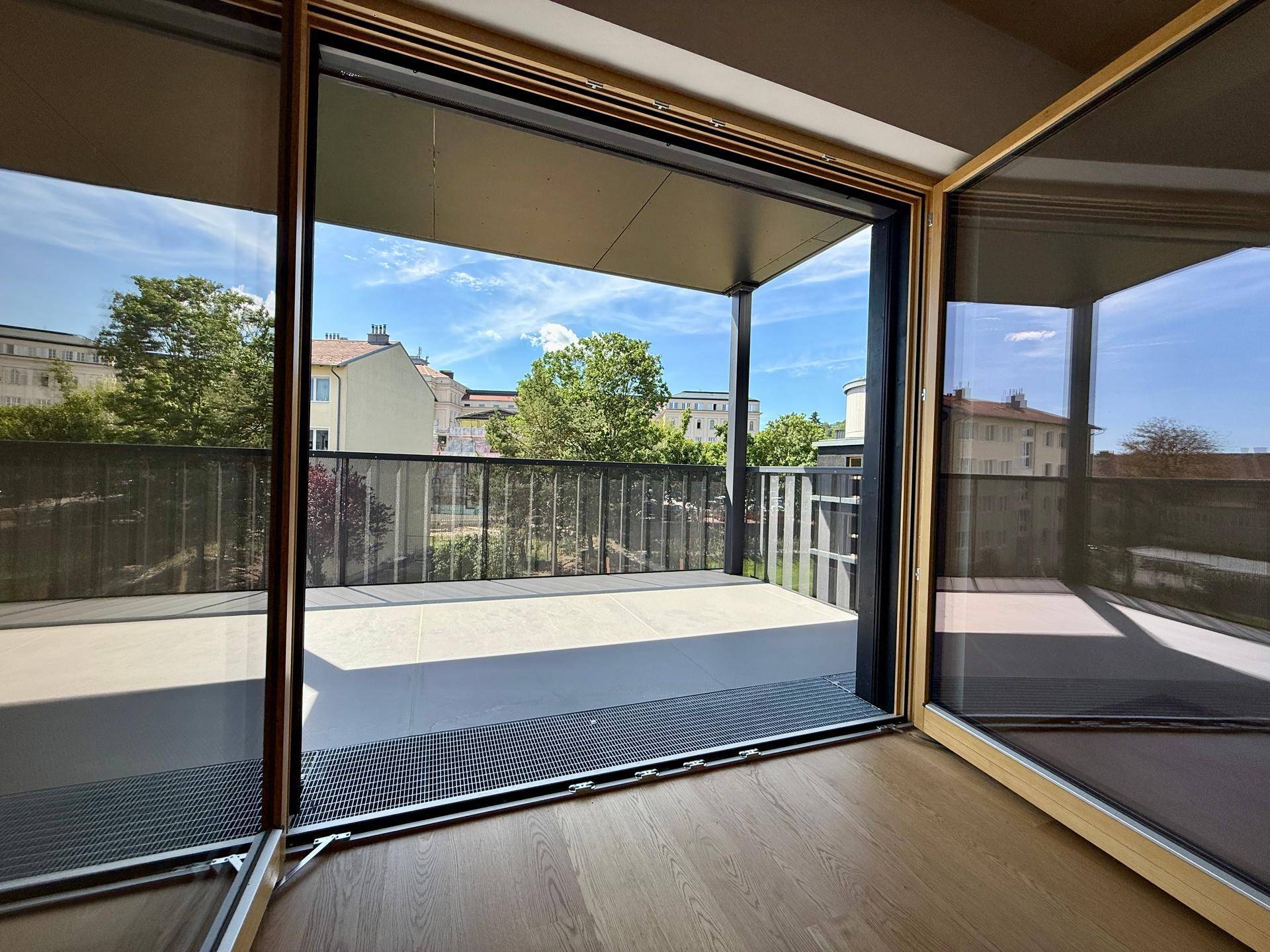 Heller Wohnraum mit Holzboden und großen Schiebetüren, die zu einem Balkon mit Stadt- und Grünblick führen.