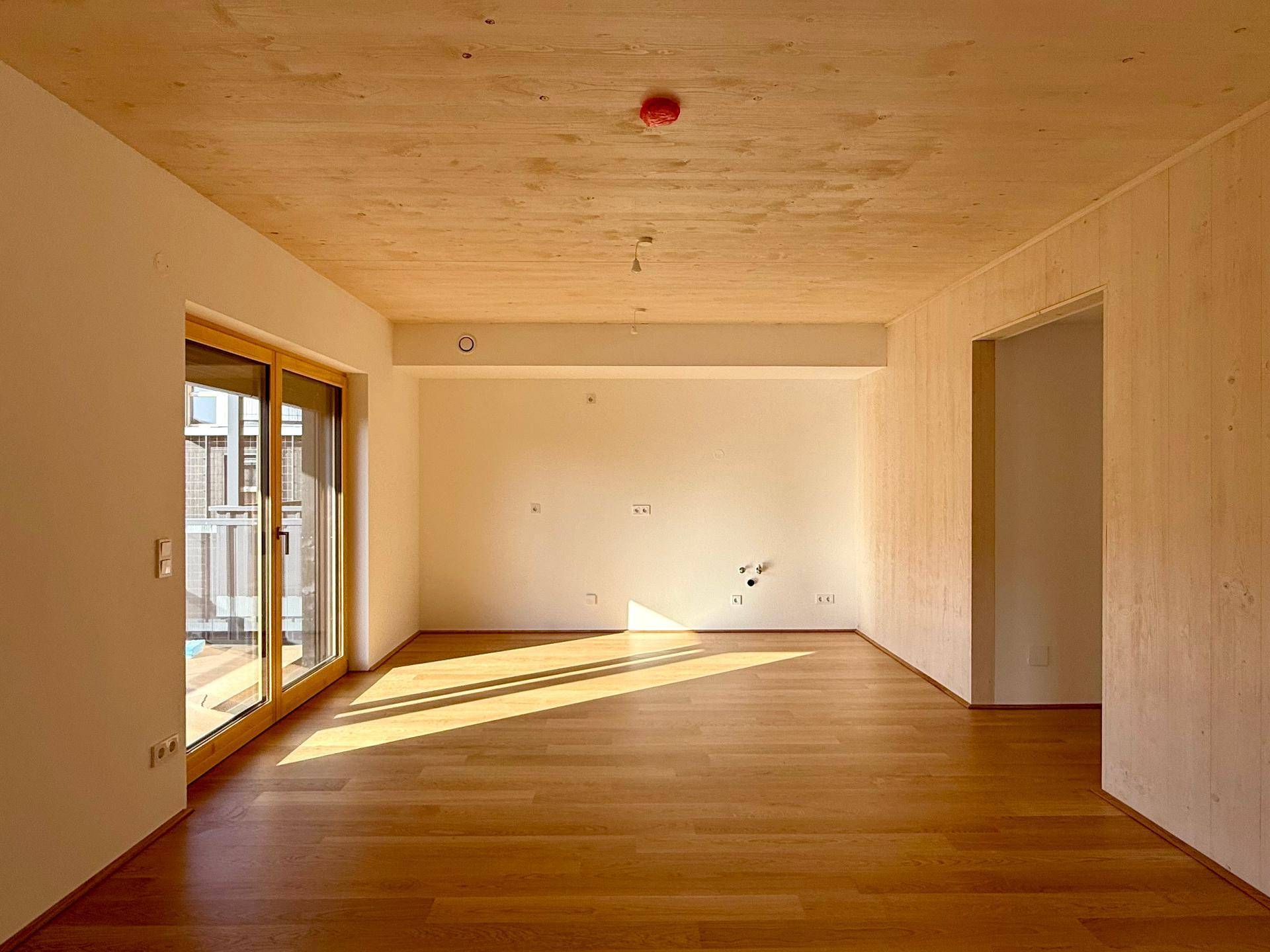 Geräumiger Wohnbereich mit Holzboden, Holzdecke und großer Schiebetür zum Außenbereich.