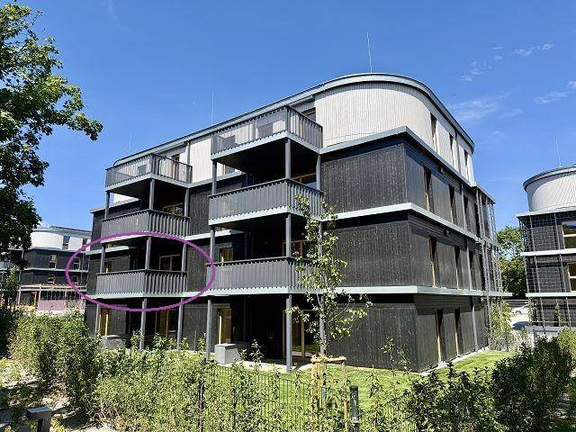 Neubau-Wohngebäude mit zeitgenössischer Architektur und mehreren Balkonen, eingebettet in eine grüne Umgebung.