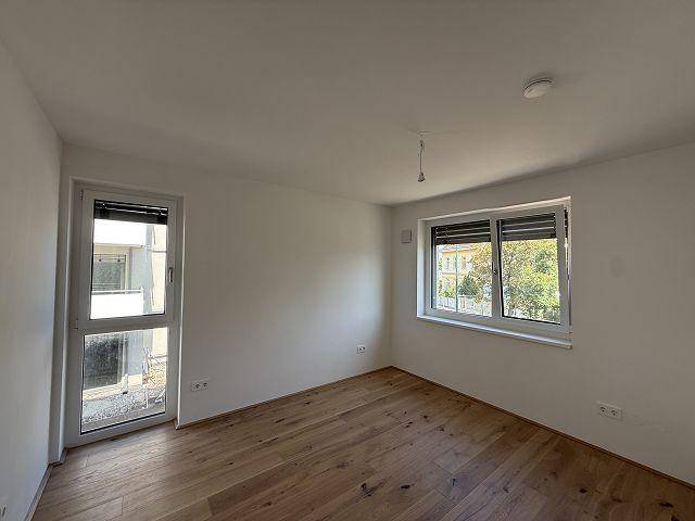 Schlafzimmer mit Holzboden und Zugang zu einem kleinen Außenbereich oder Balkon, sehr hell.