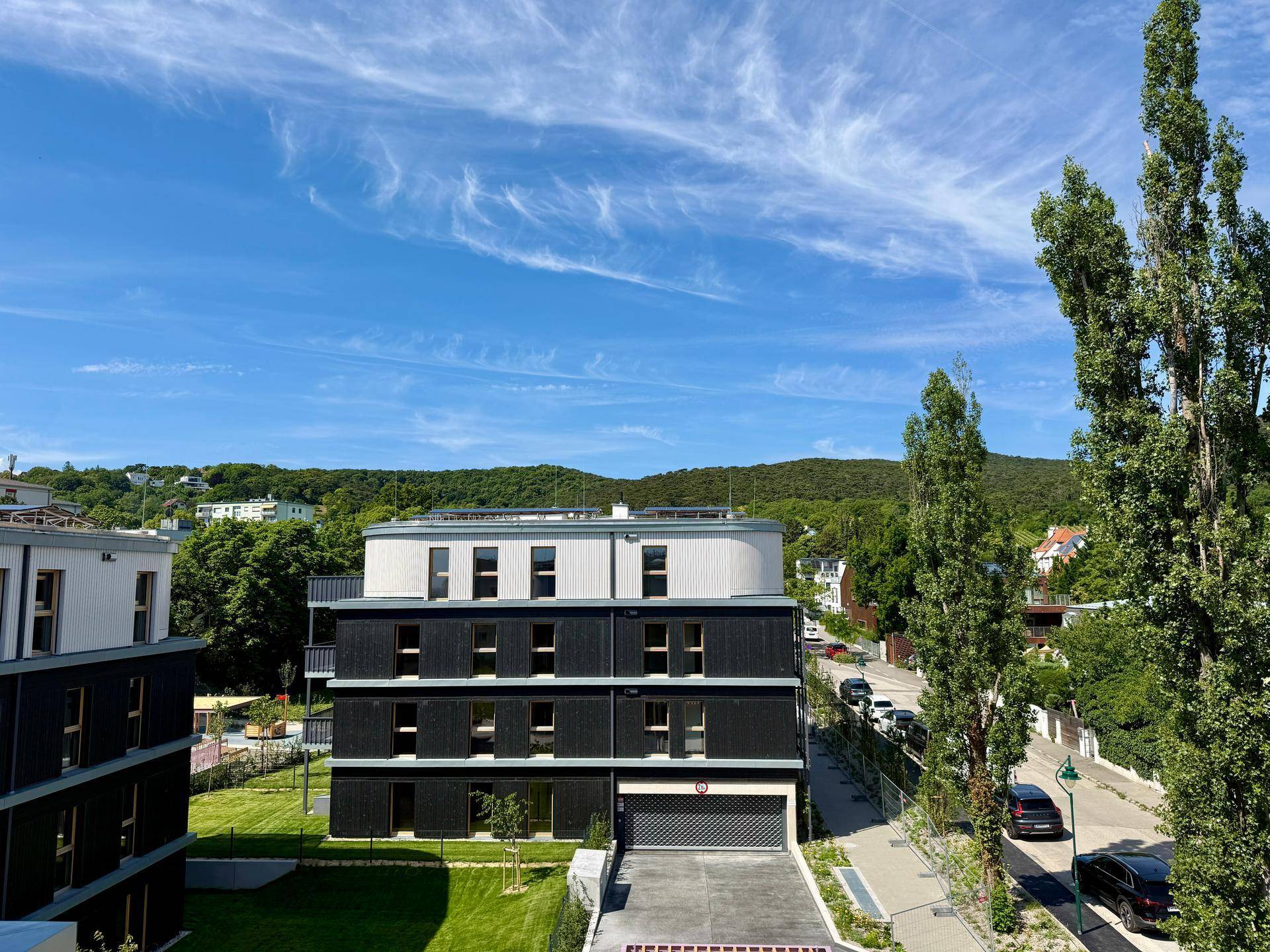 Blick vom Balkon auf ein modernes Wohngebäude mit dunkler Fassade und grüner Umgebung.