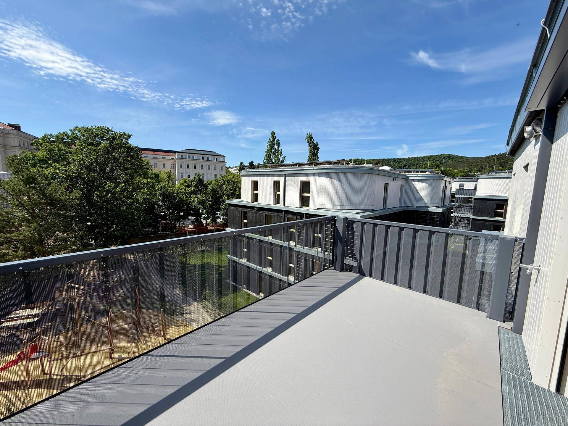 Heller Balkon mit Blick auf einen Spielplatz und die moderne Wohnanlage.