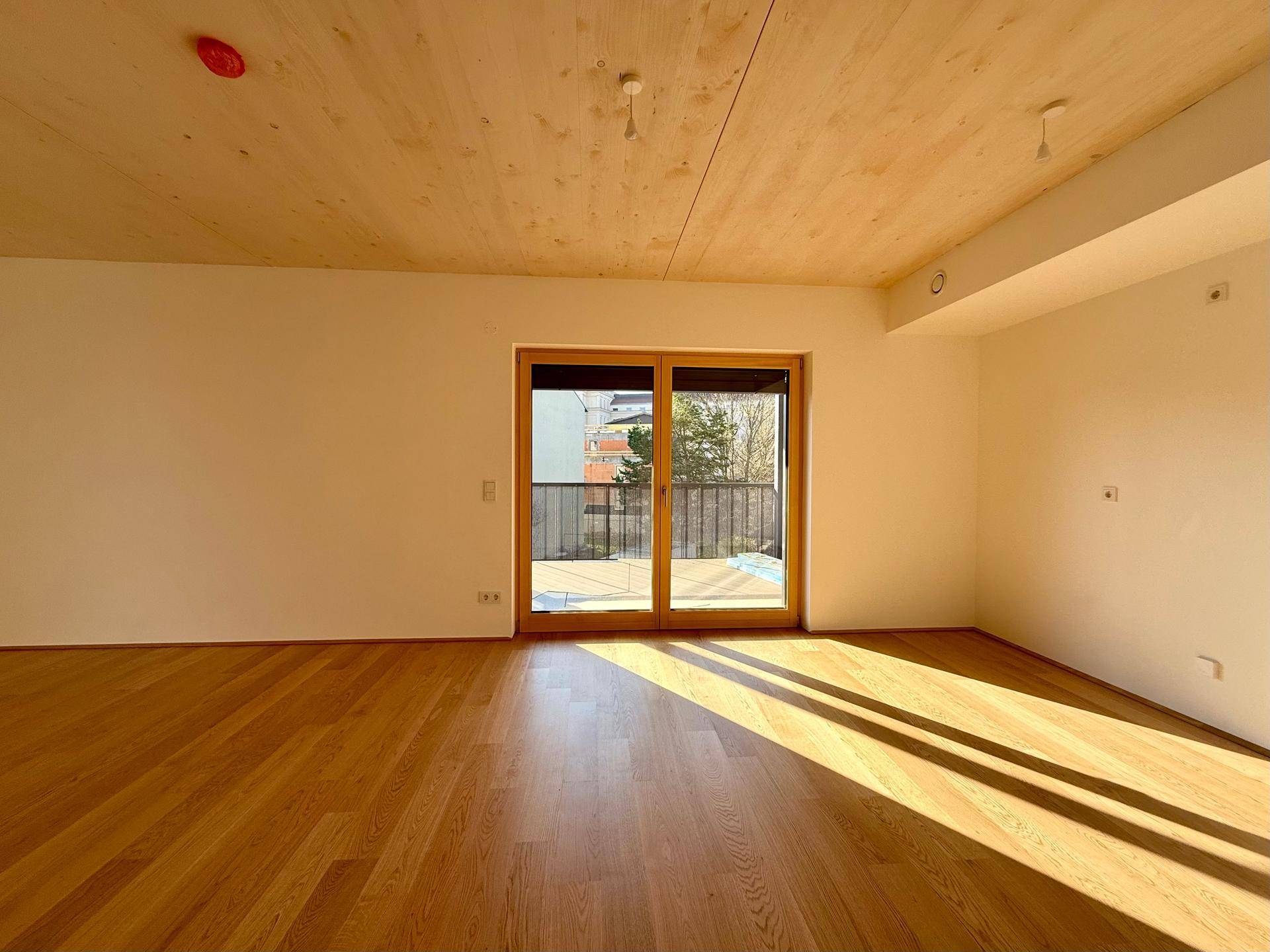 Lichtdurchfluteter Wohnbereich mit Holzboden und Zugang zu einem Balkon oder einer Terrasse.