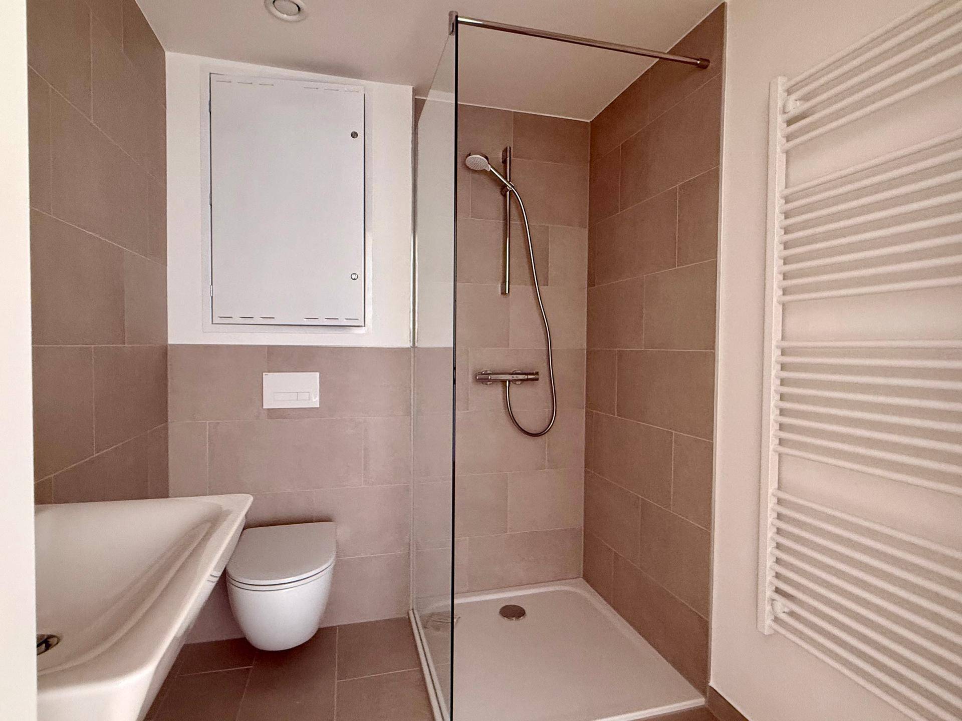 Modernes Badezimmer mit beigefarbenen Fliesen, wandhängendem WC und einer Duschkabine.