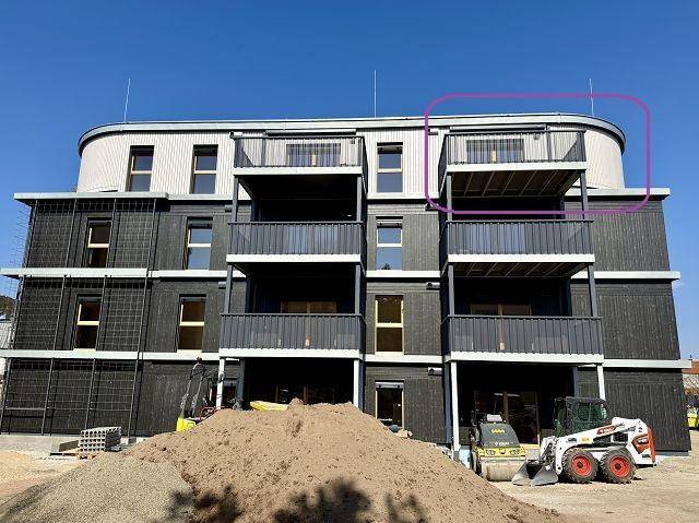 Neubau-Wohngebäude mit dunkler Fassade und mehreren Balkonen, umgeben von Baustellenaktivitäten.