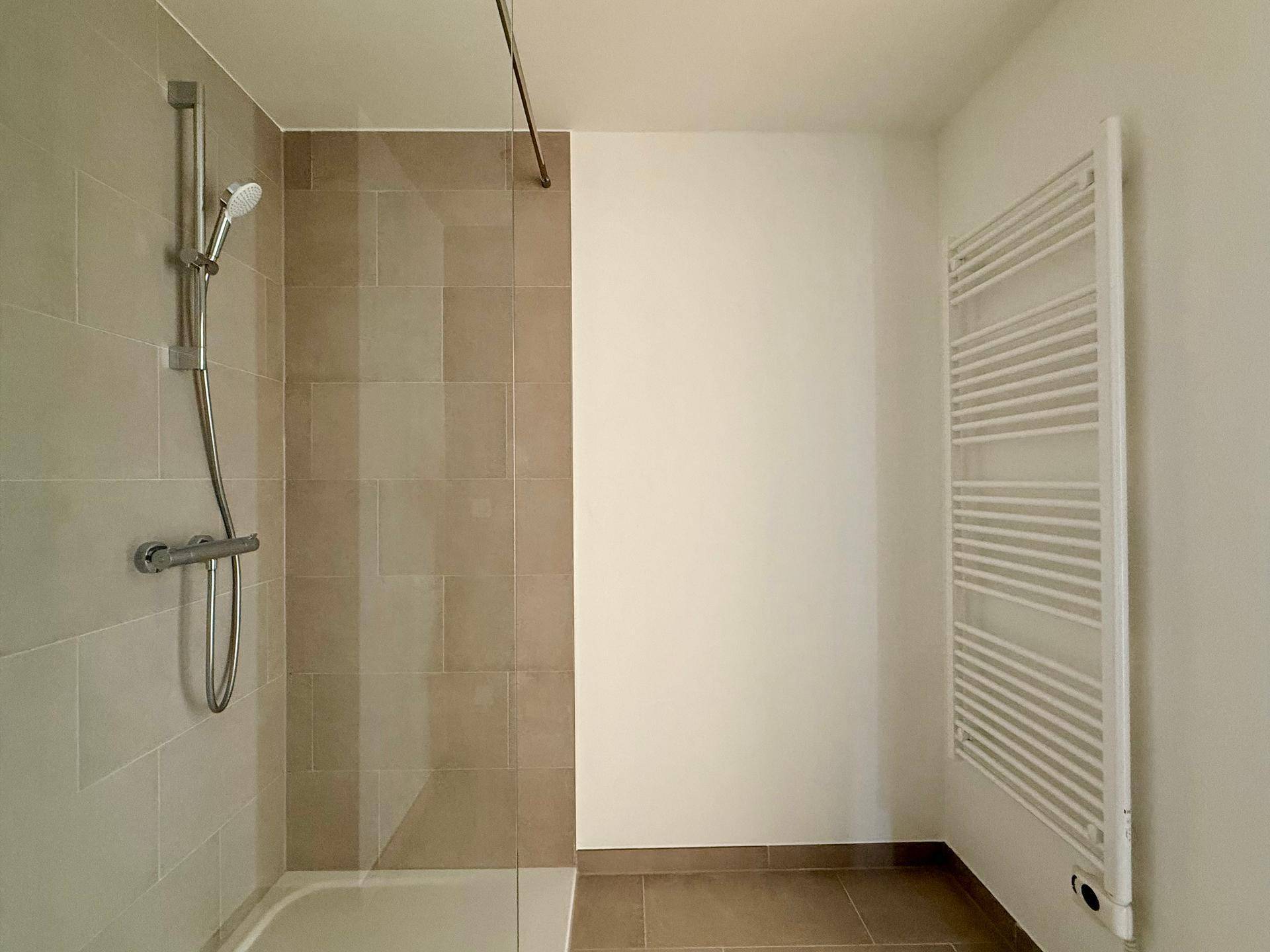 Duschbereich im Badezimmer mit beigefarbenen Fliesen und beheiztem Handtuchhalter.