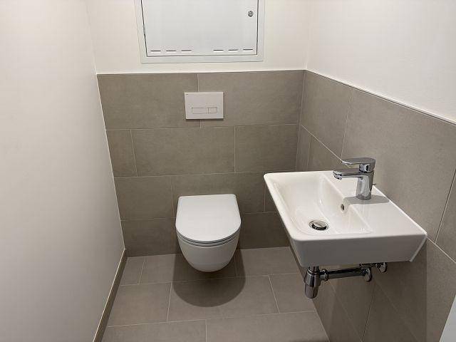 Separates Gäste-WC mit wandhängender Toilette und kleinem Waschbecken, modern gefliest.