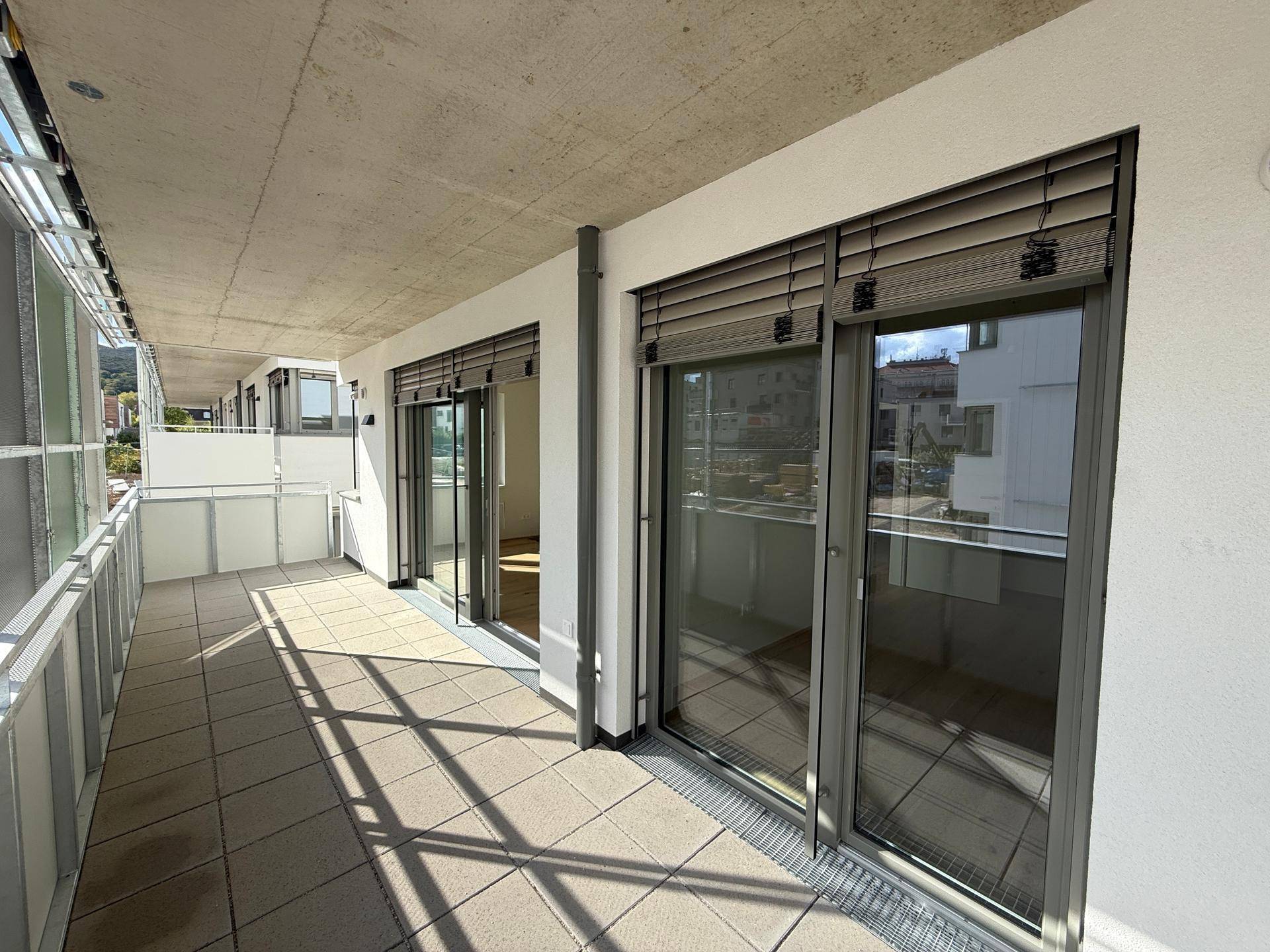 Langer Balkon mit Fliesenboden und Jalousien, bietet viel Sonnenlicht.