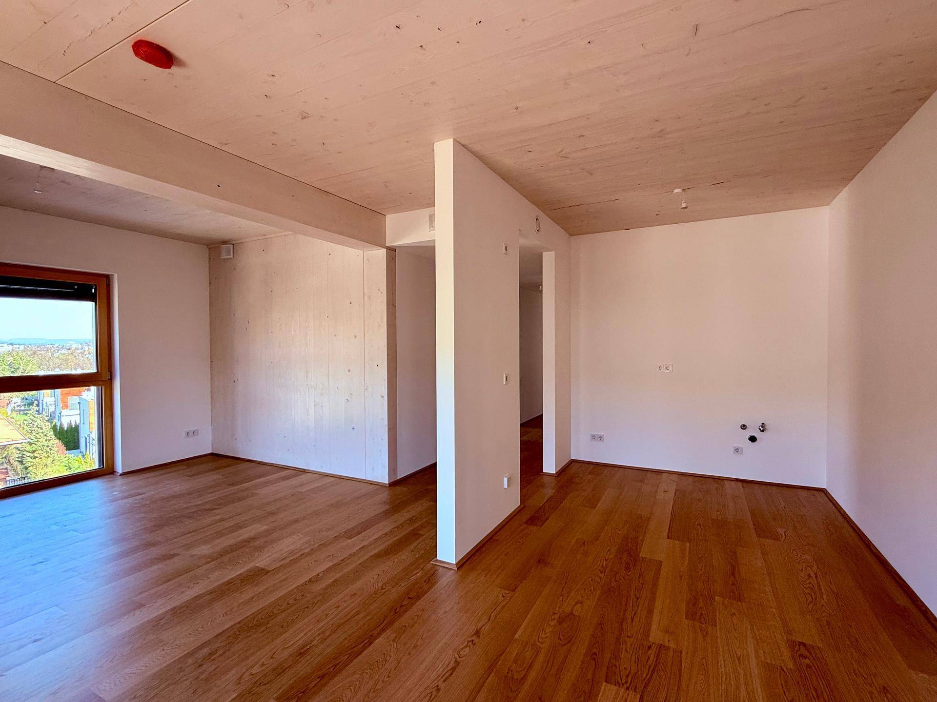 Offener Raum mit Holzboden und Anschlüssen für eine zukünftige Einbauküche in einem Neubau.