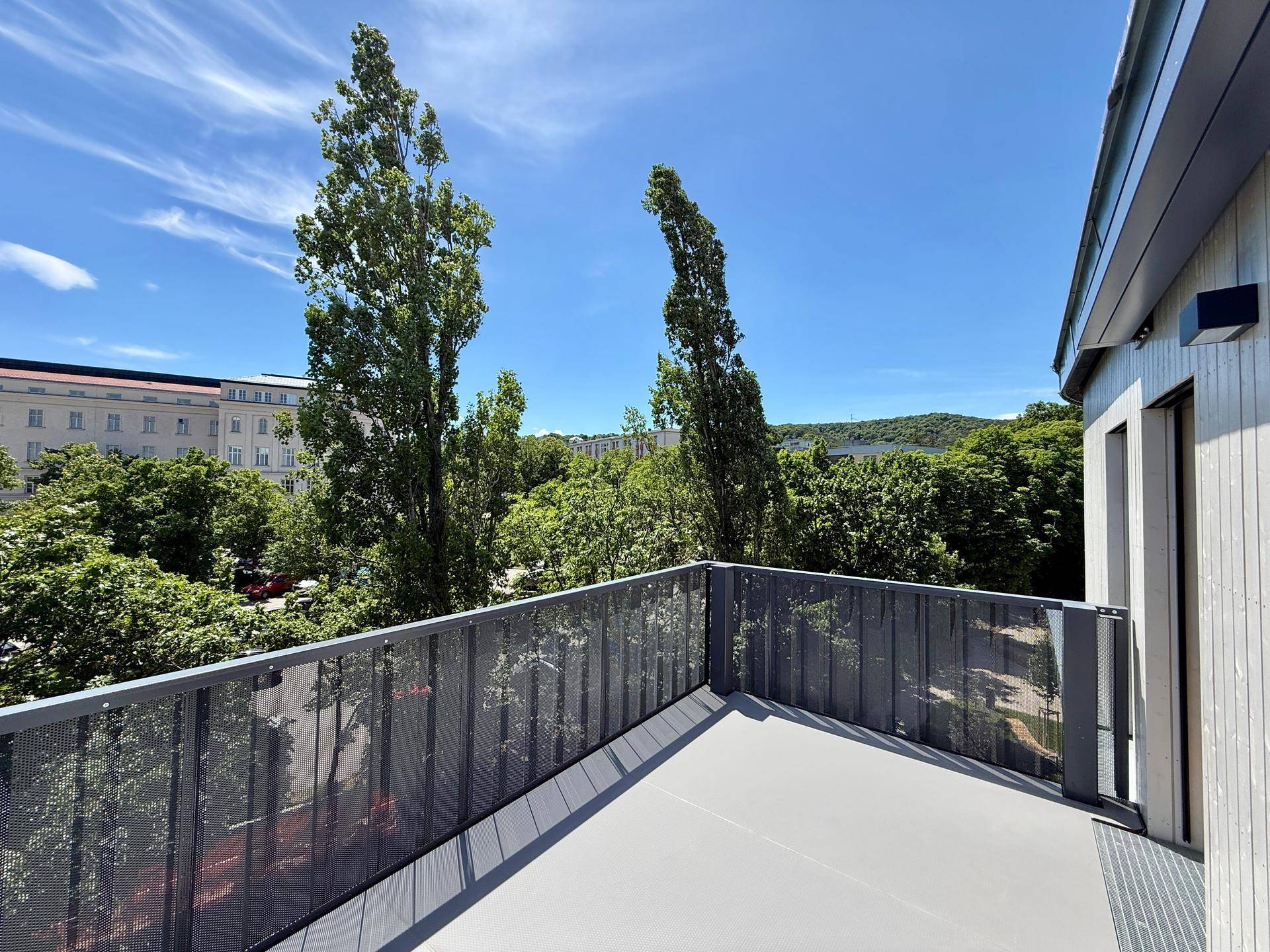 Weitläufiger Balkon mit Blick auf hohe Bäume und die städtische Architektur in der Ferne.