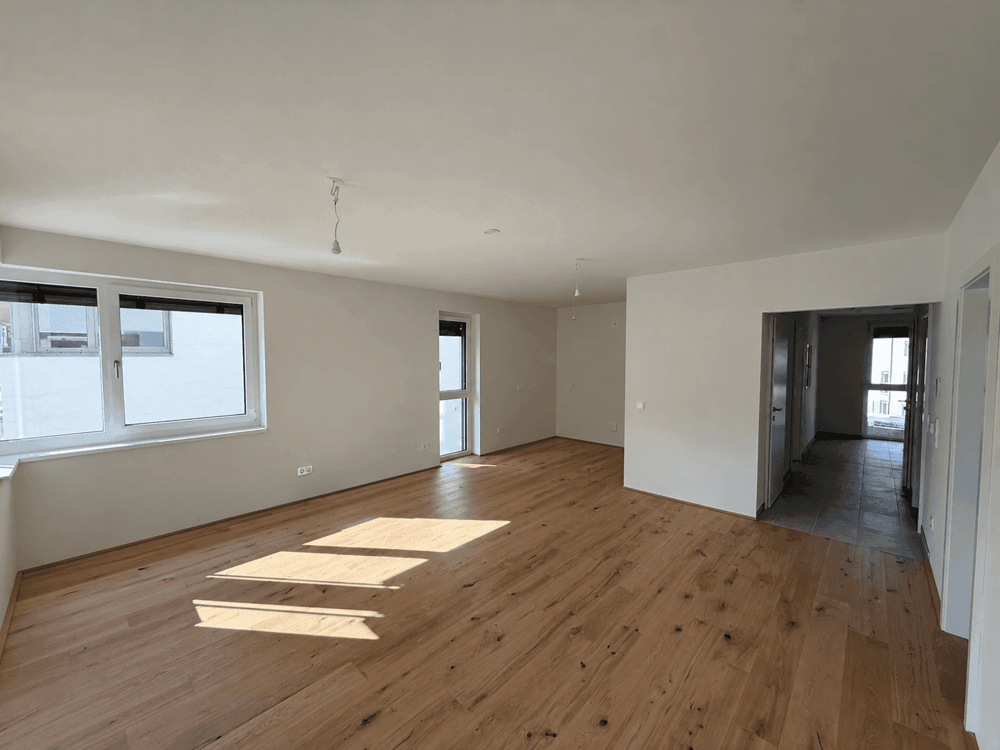 Geräumiges, leeres Wohnzimmer mit Holzboden und großen Fenstern, bereit zur Einrichtung.