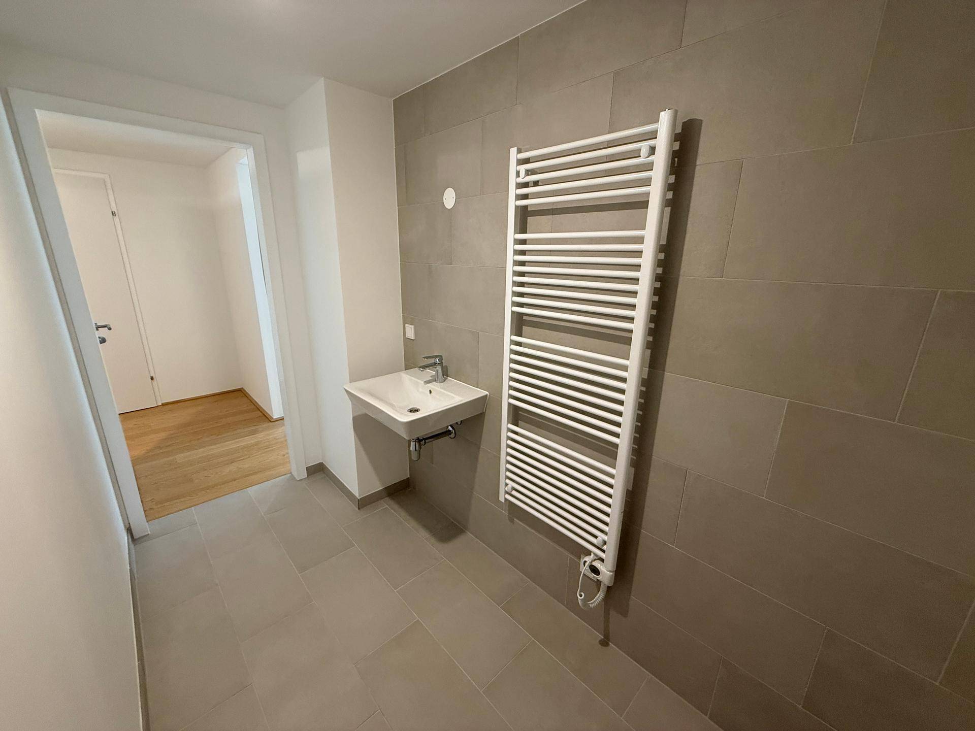 Helles Badezimmer mit modernen grauen Fliesen, Waschbecken und praktischem Handtuchheizkörper.
