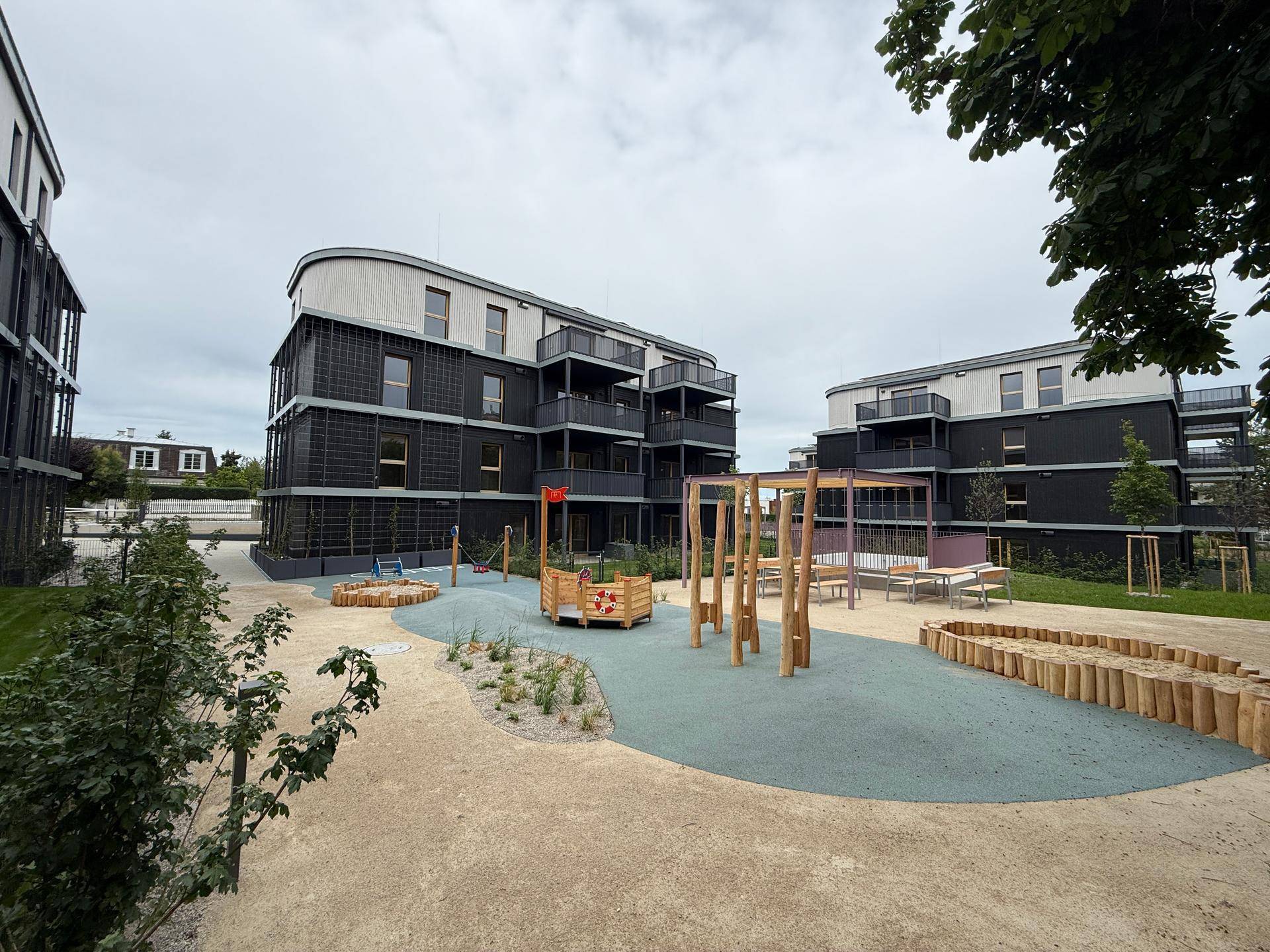 Moderne Wohngebäude mit dunklen Fassaden und einem gemeinschaftlichen Kinderspielplatz im Vordergrund.