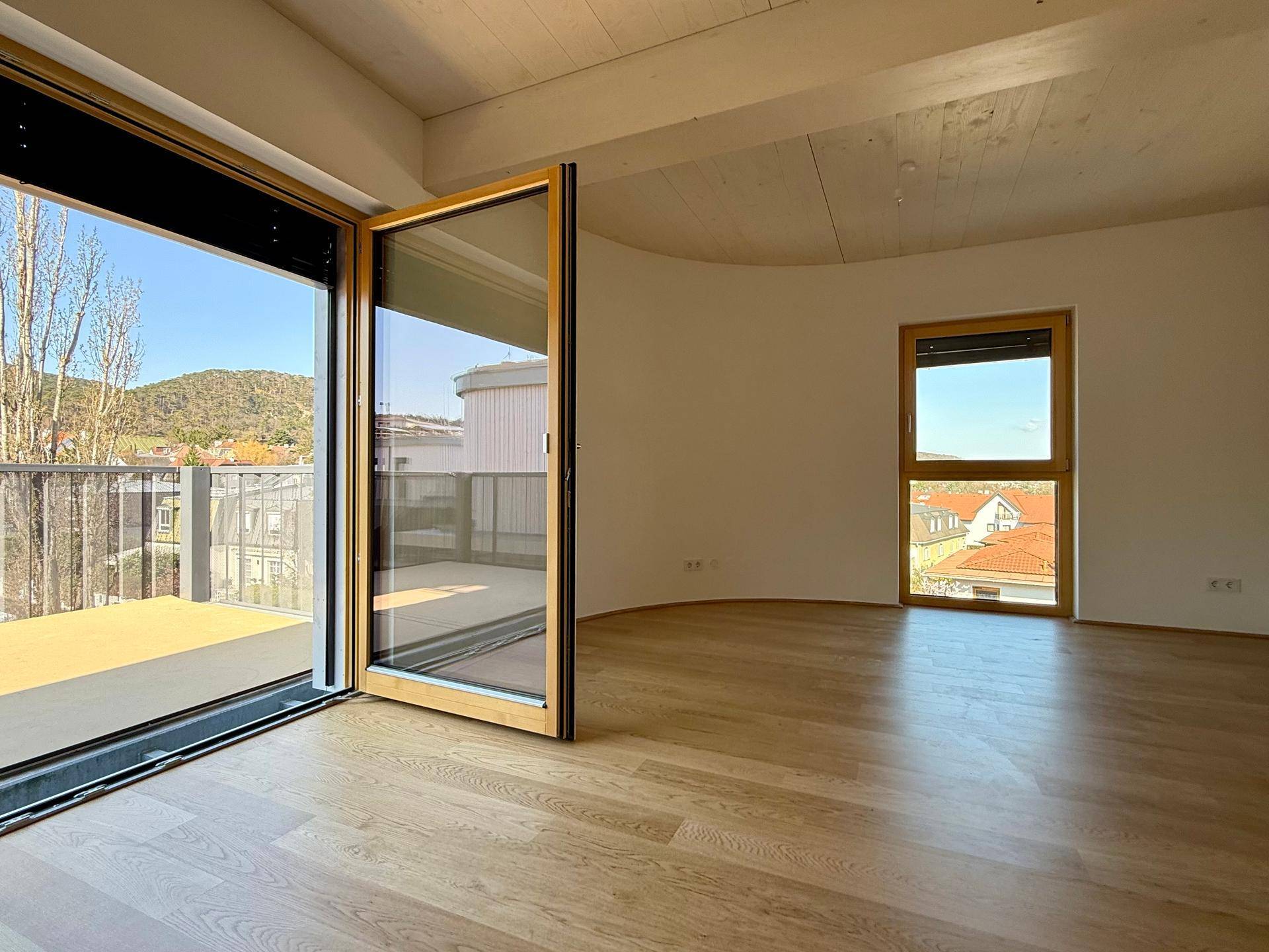 Heller Wohnraum mit Holzboden, großen Fenstern und Zugang zu einem sonnigen Balkon mit Aussicht.