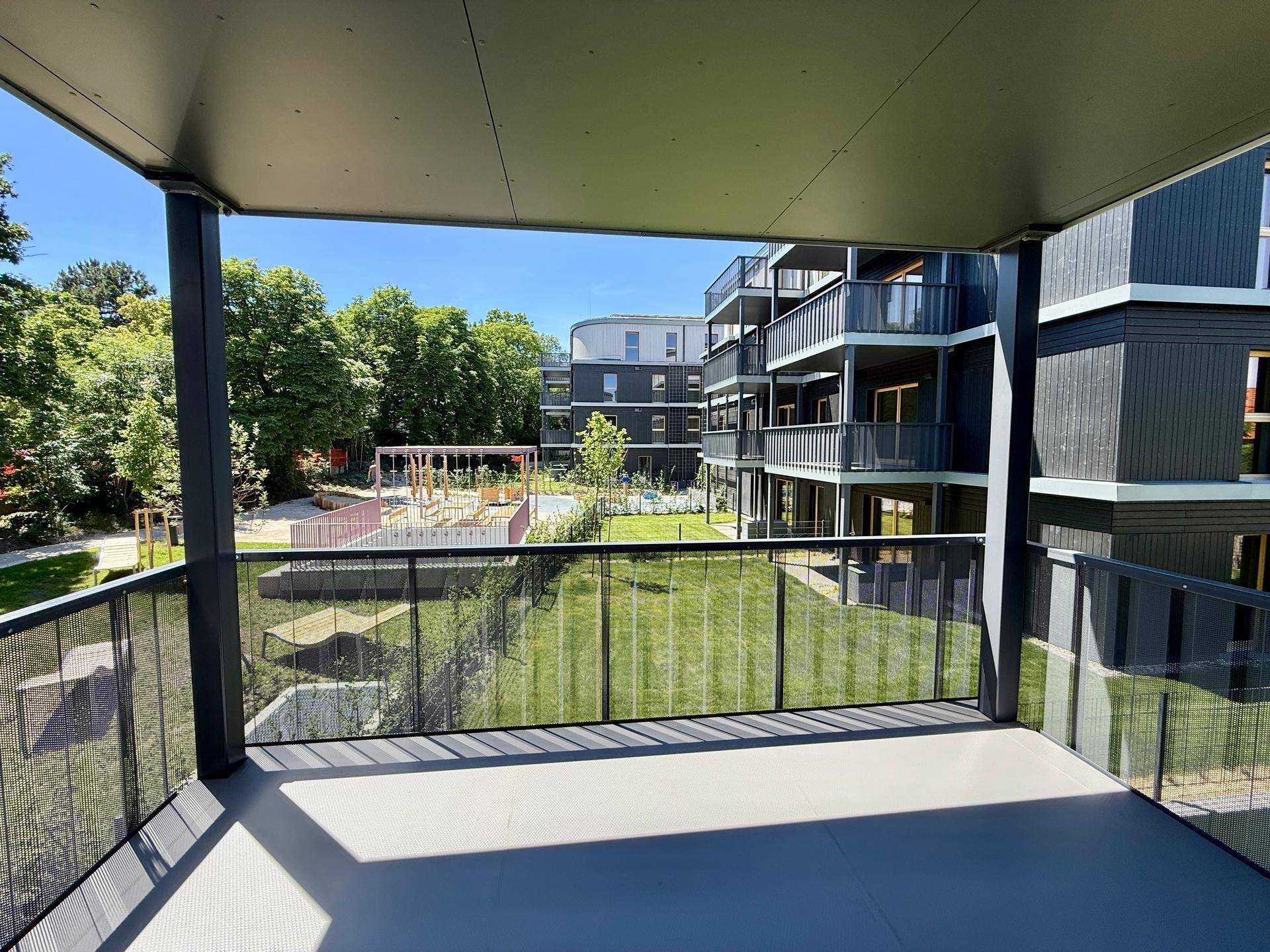 Geräumiger Balkon mit Blick auf den grünen Innenhof, einen Spielplatz und moderne Wohngebäude.