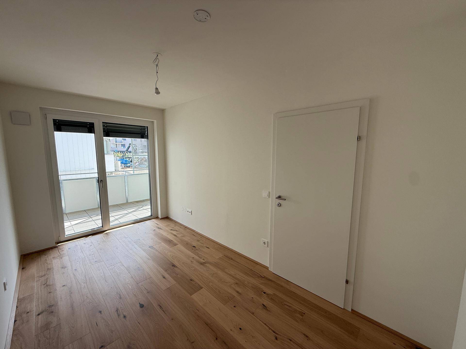 Leeres Schlafzimmer mit Holzboden und direktem Zugang zum Balkon.