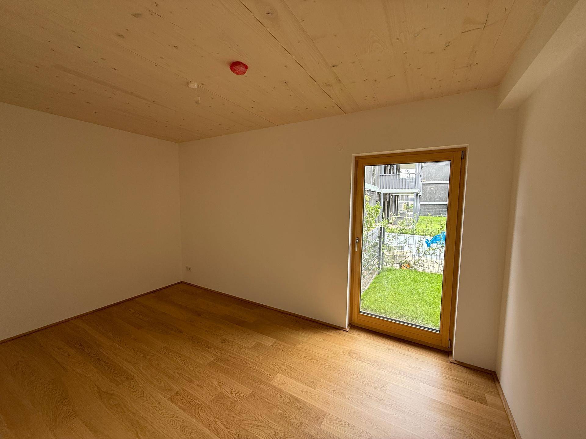 Gemütliches Zimmer mit Holzboden und Holzdecke, großen Fenstern und Blick auf den Außenbereich.