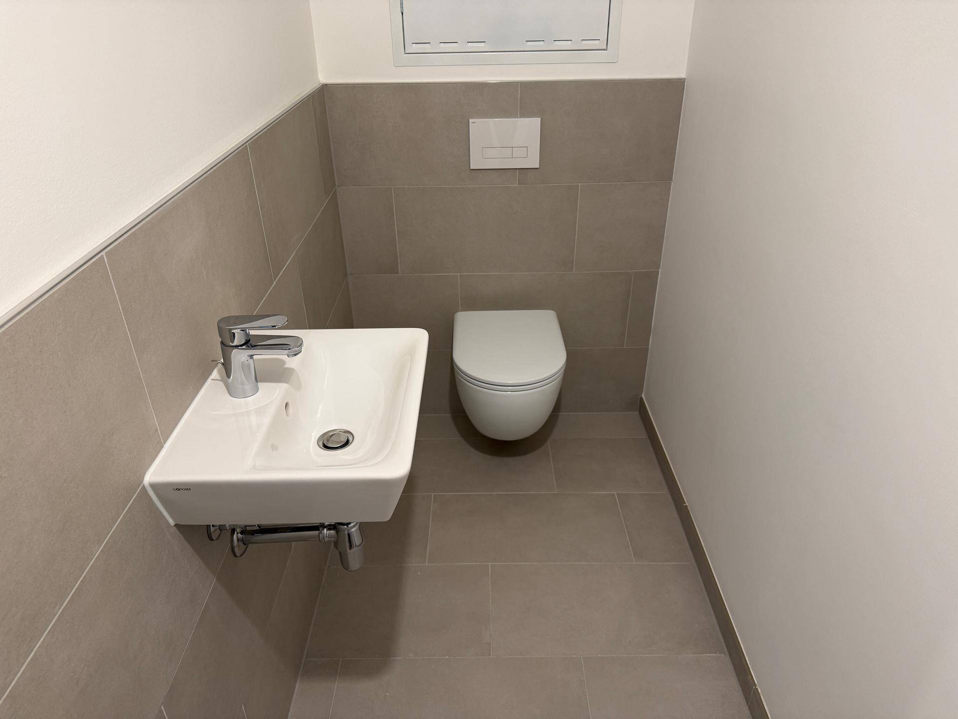 Funktionales Gäste-WC mit modernen grauen Fliesen, wandhängendem WC und kleinem Waschbecken.