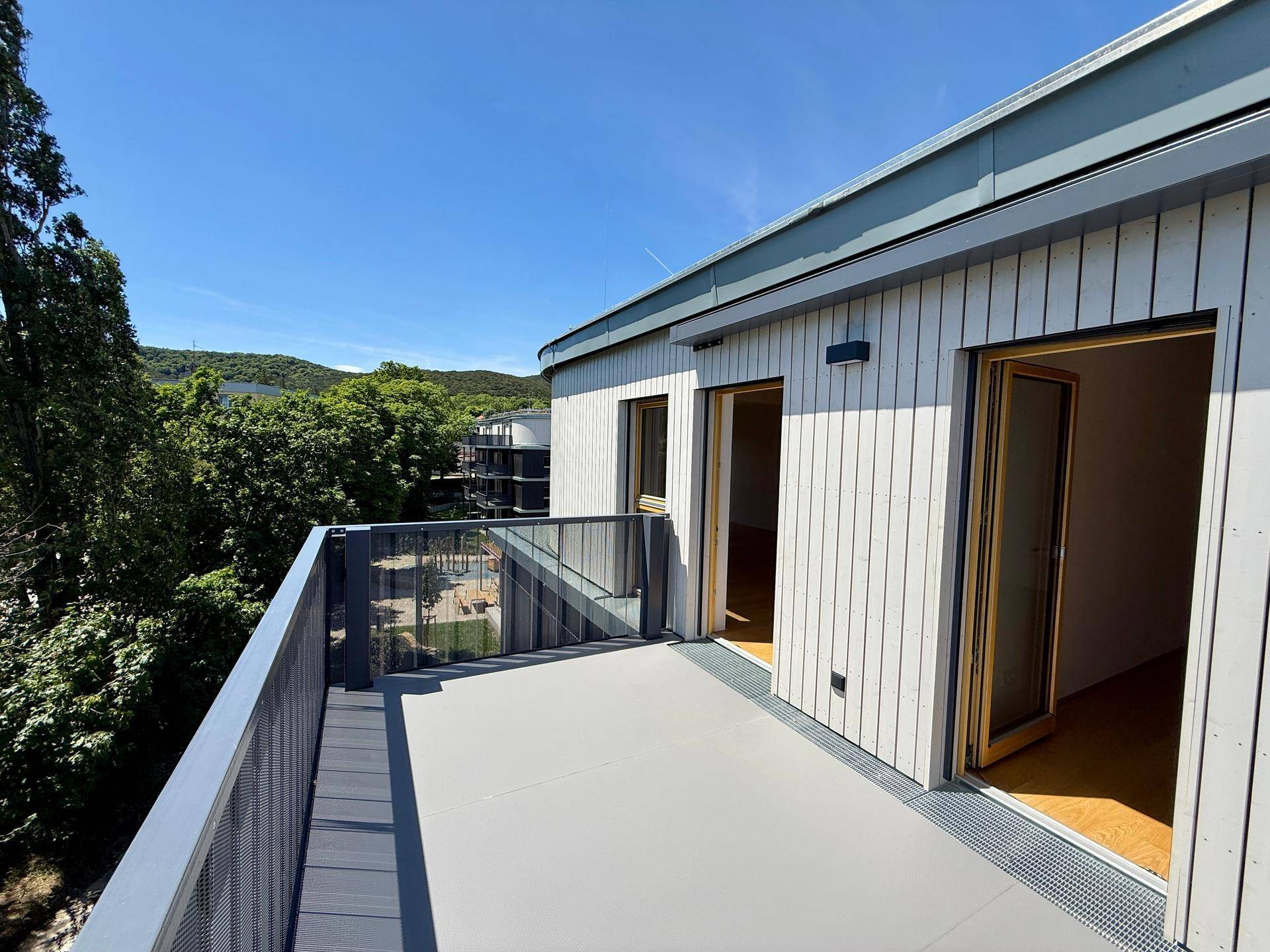 Heller Balkon mit Zugang zu den Innenräumen und Panoramablick auf die grüne Umgebung.