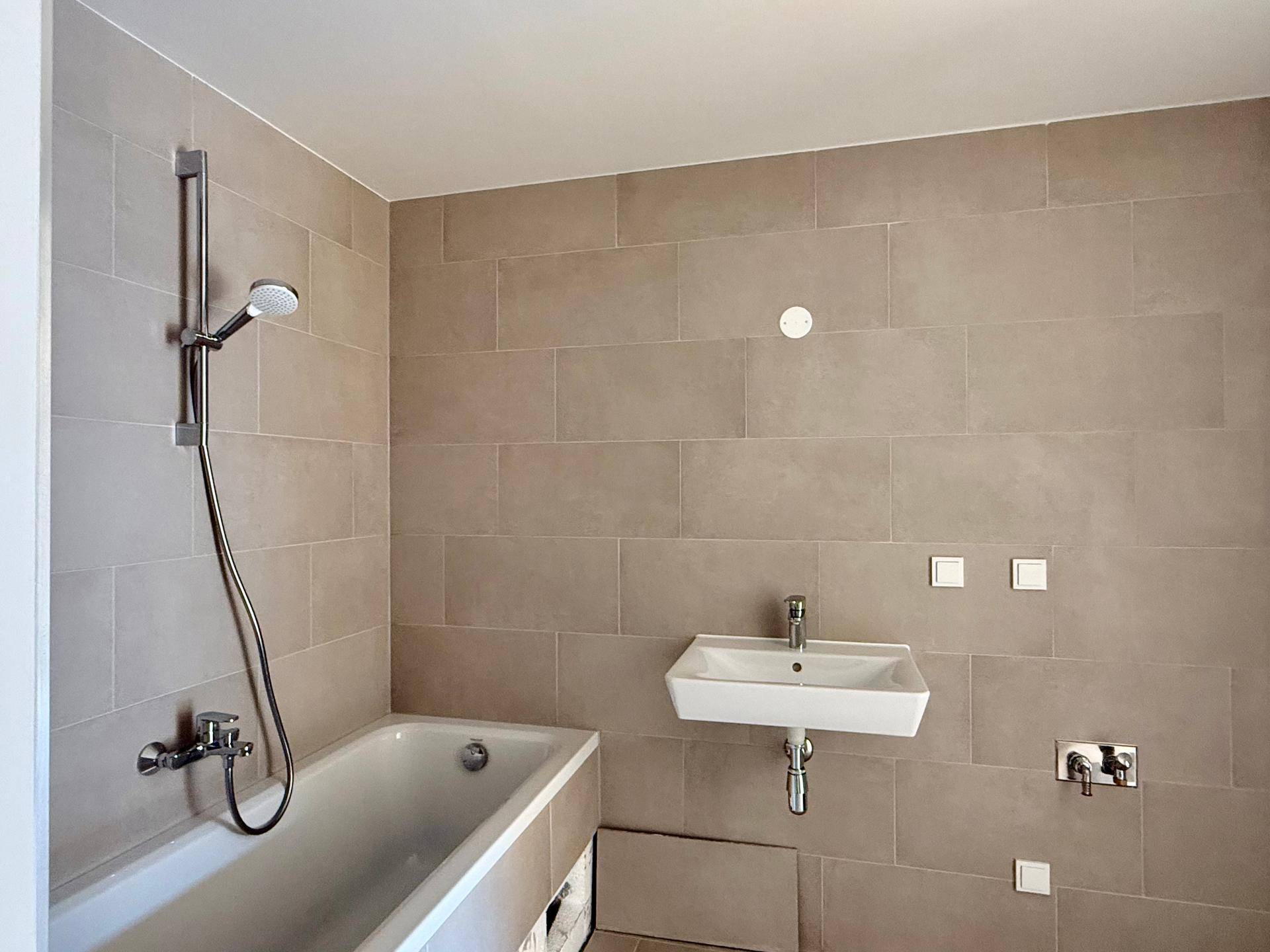 Modernes Badezimmer mit beigefarbenen Fliesen, Badewanne und Waschbecken, bereit zur Fertigstellung.