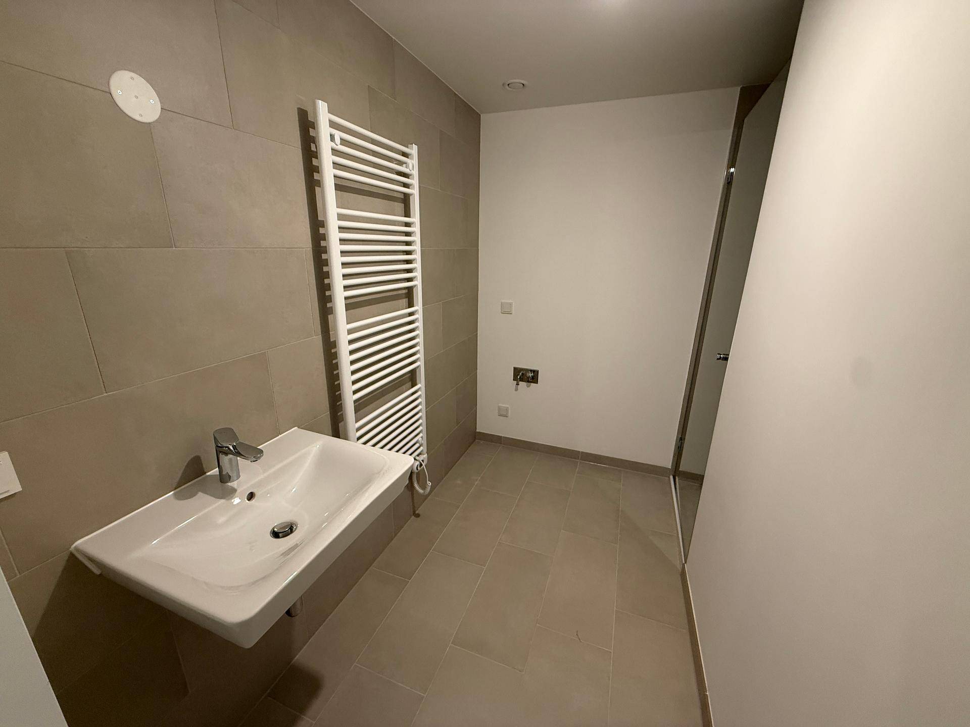 Modernes Badezimmer mit grauen Fliesen, wandhängendem Waschbecken und beheiztem Handtuchhalter.