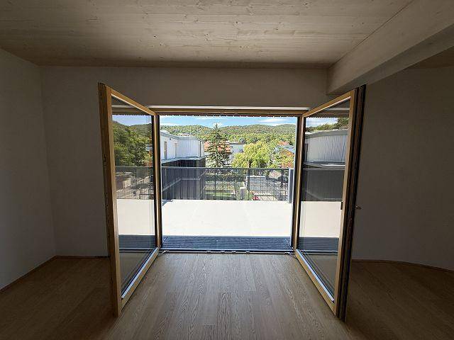 Heller Innenraum mit Holzboden und großen Fenstern, die zur Terrasse führen und weite Ausblicke bieten.